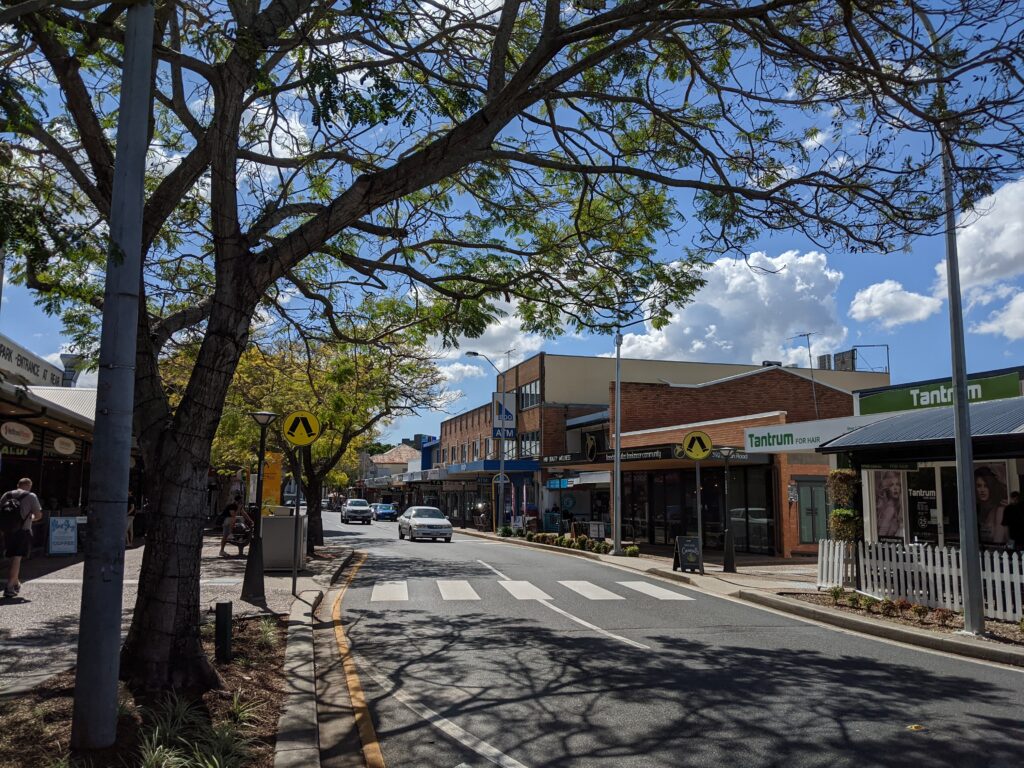 A car approaches a pedestrian crossing on a quaint, tree-lined street.