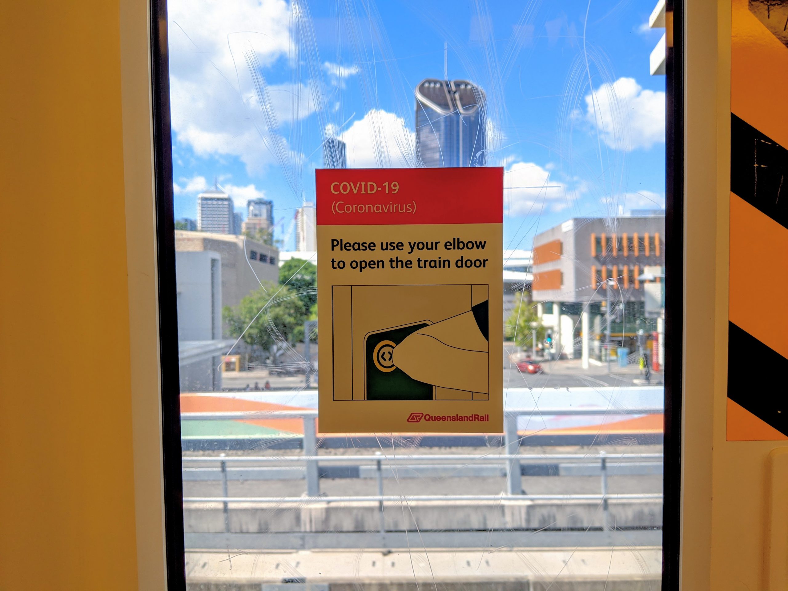 Looking out the train window. Brisbane City in the background. Sticker on the window: "Please use your elbow to open the train door"