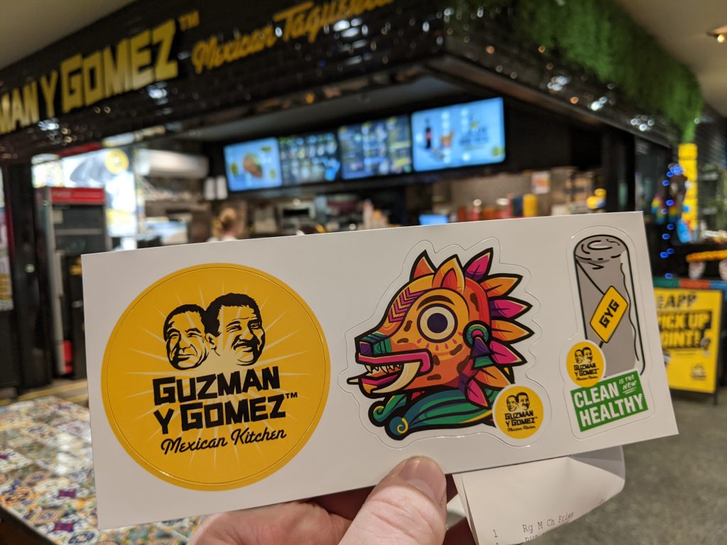 A set of three brightly coloured magnets, with a Guzman y Gomez counter in the background.
