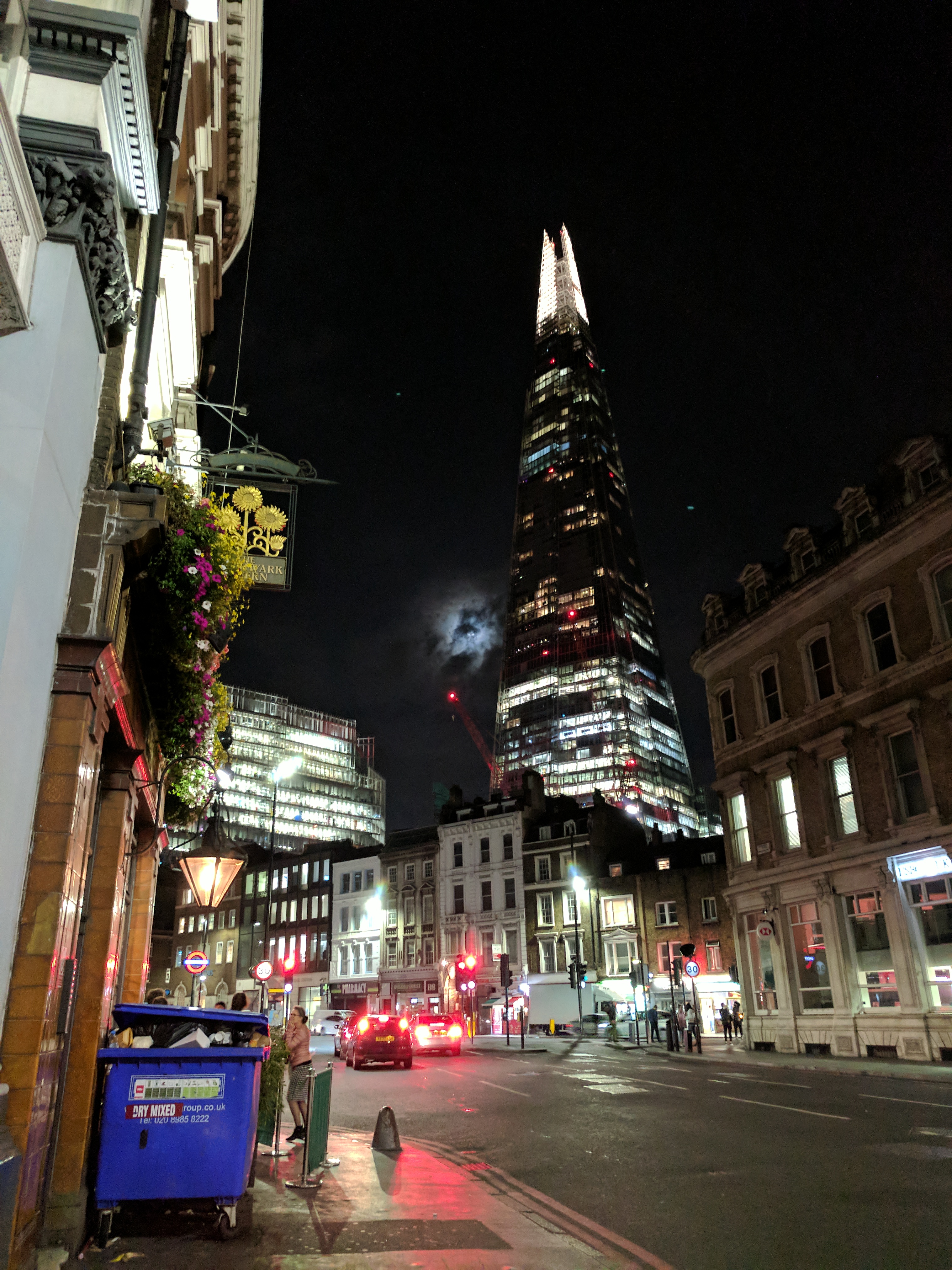 Looking up at The Shard, the moon poking through the clouds, and an overflowing dumpster on the street.