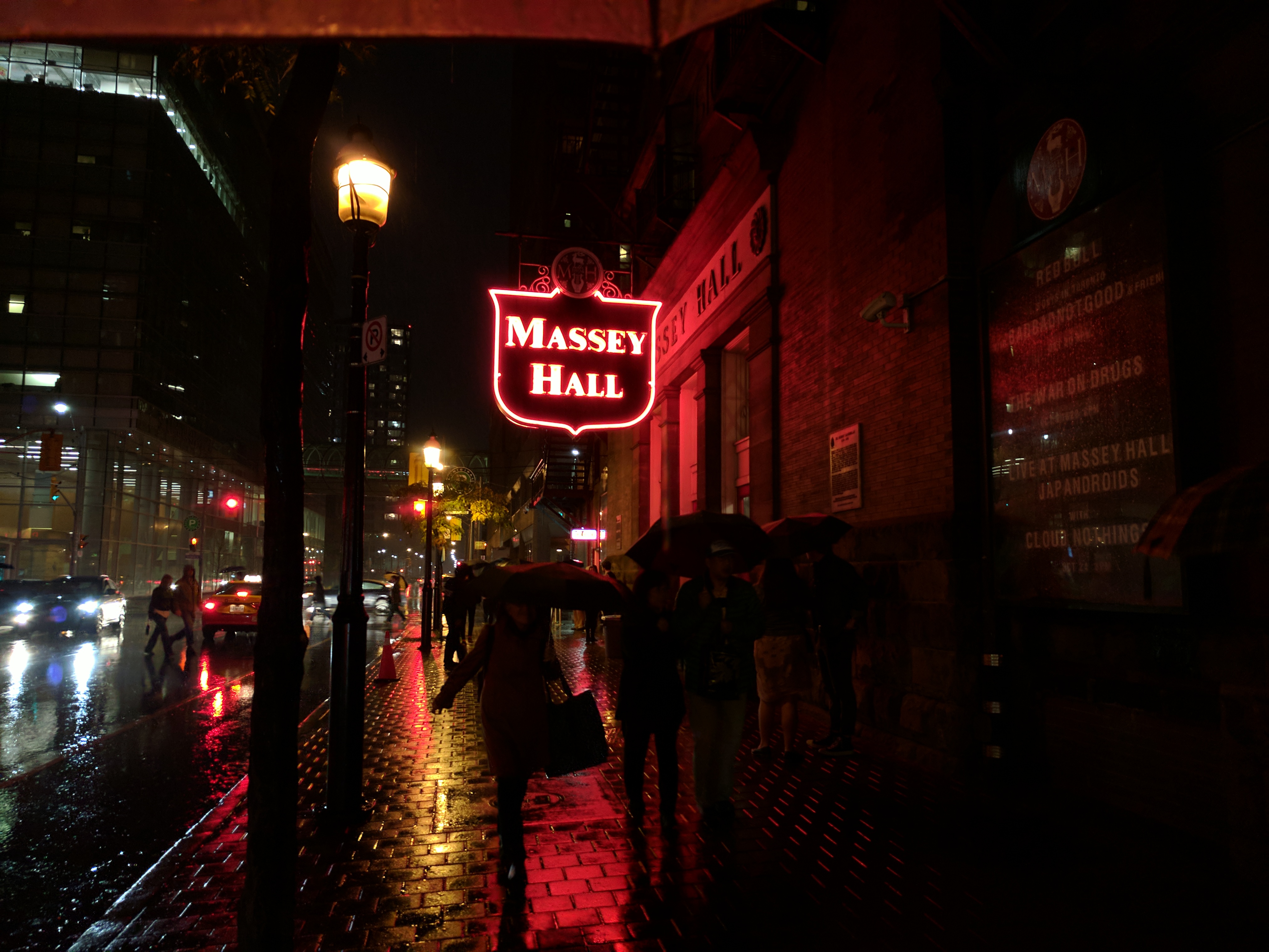 Massey Hall from outside, illuminated in red neon. There are reflections from all the wet.