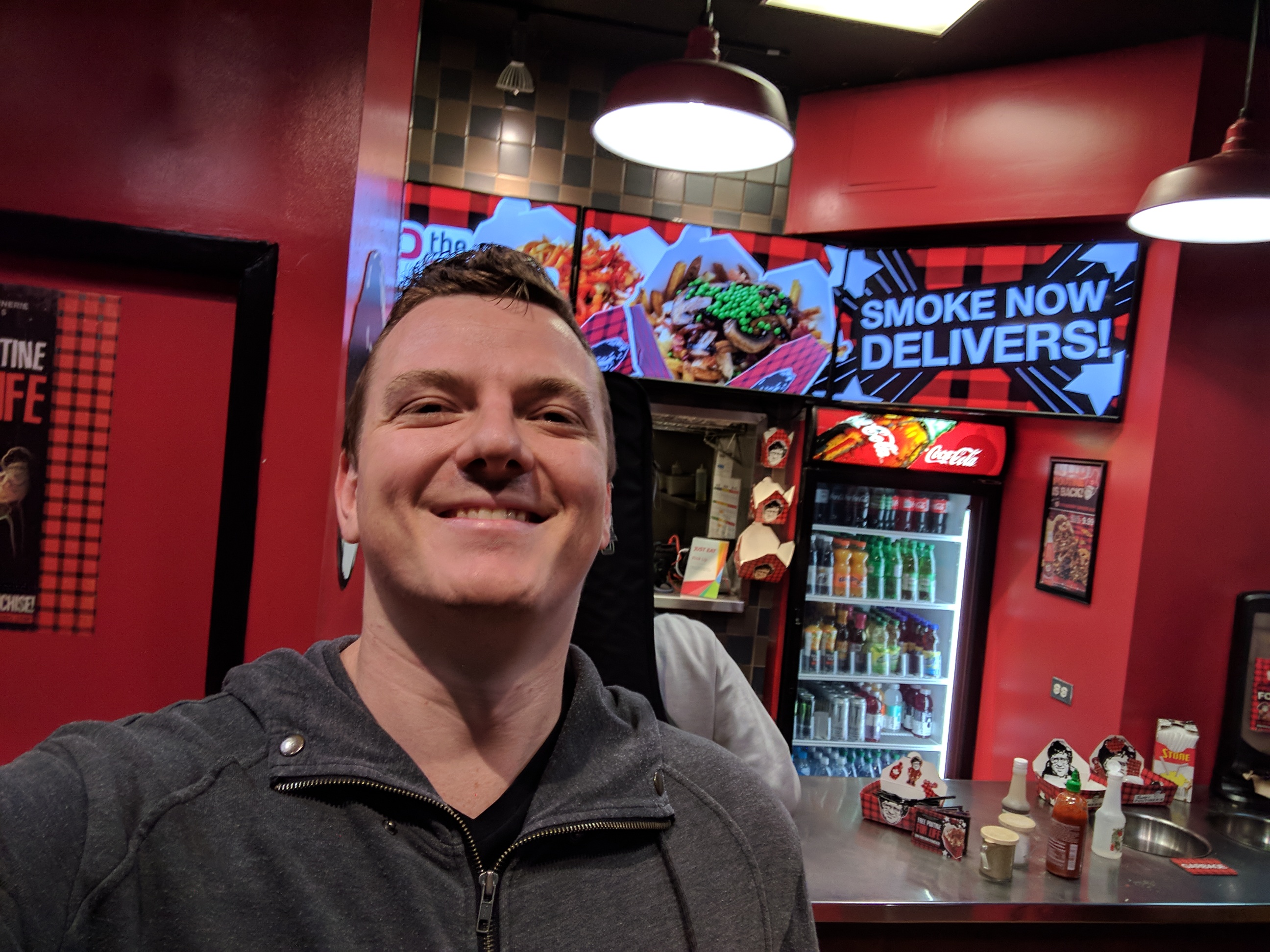 Me looking super happy at the poutine place. The display reads "Smoke now delivers!"