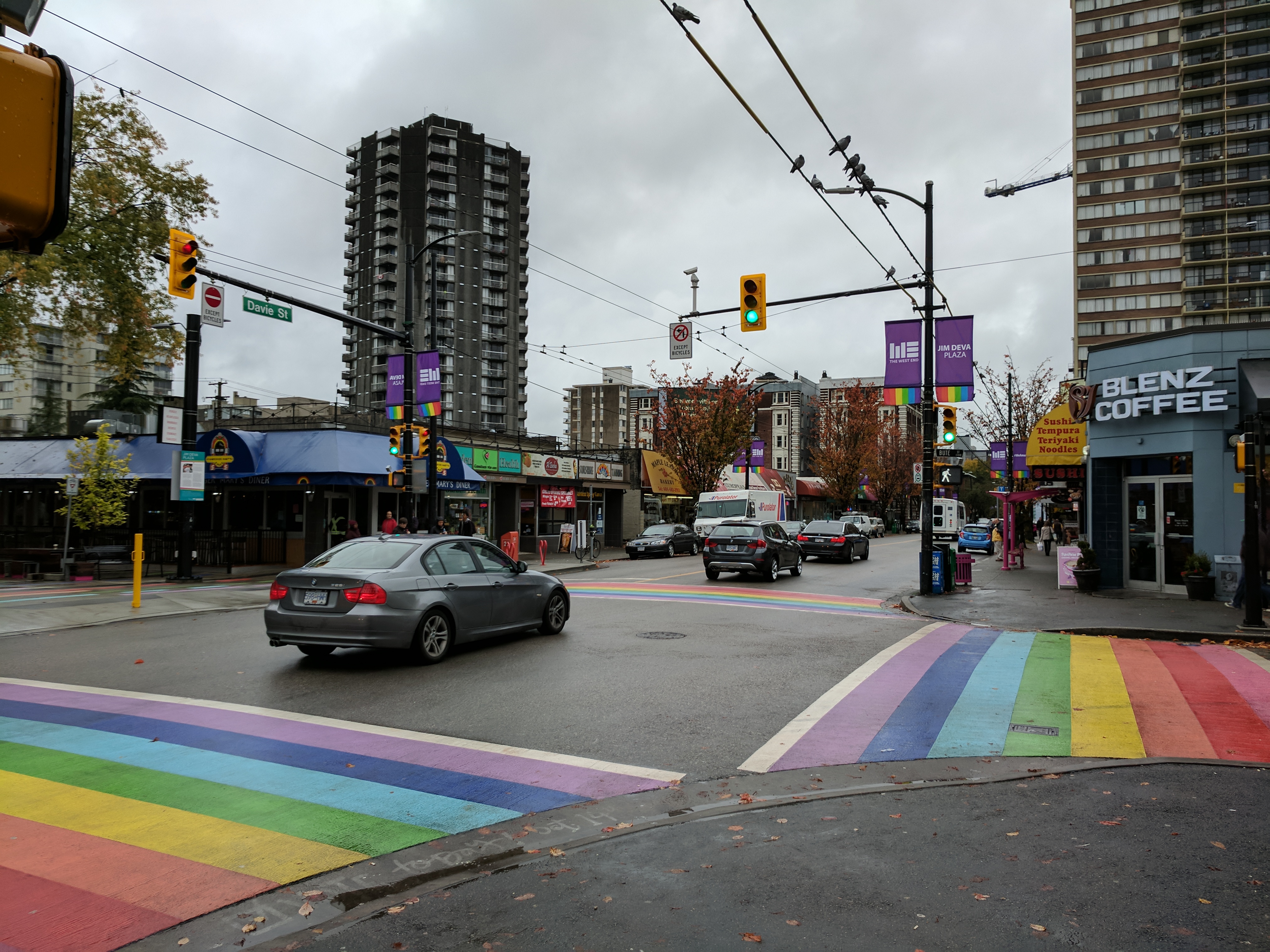 Rainbow crosswalk at the corner of Bute and Davie. There are cars driving through the intersection and a Blenz Coffee on one corner.