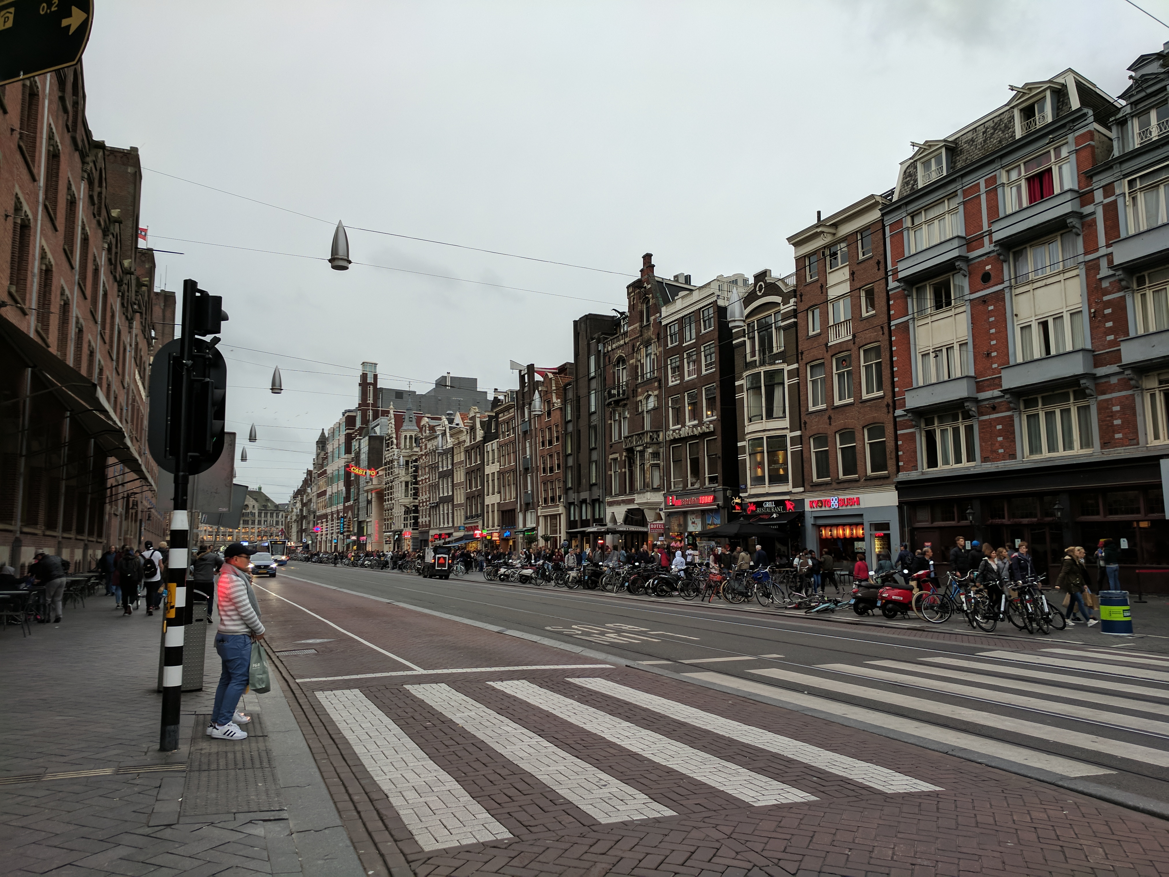 A grey sky, extremely drab Amsterdam street. The architecture is the only thing of note because everything else looks miserable.