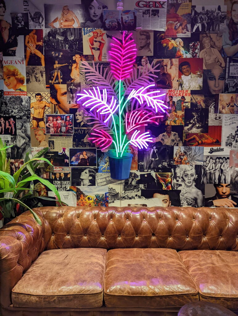 The neon flower lounge, surrounded by plants, a brown leather couch and a wall mosaic of pop culture