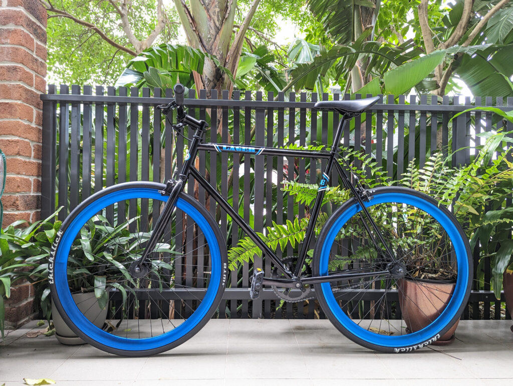 A black bike with neon blue rims in front of a garden.