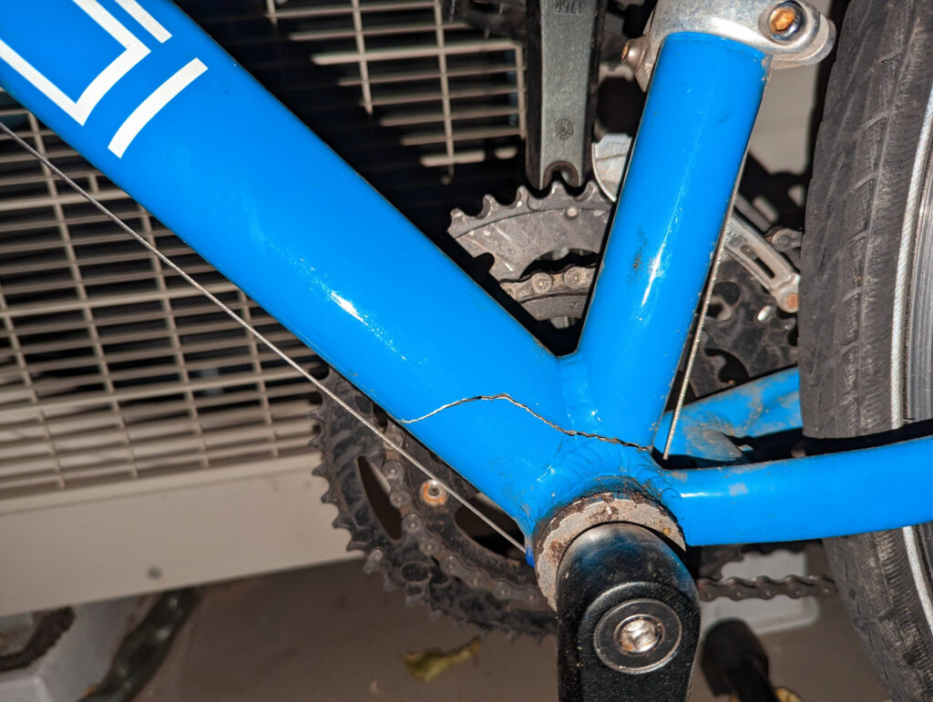 A blue bike frame with a crack running horizontally above the bottom bracket. You can see through it.