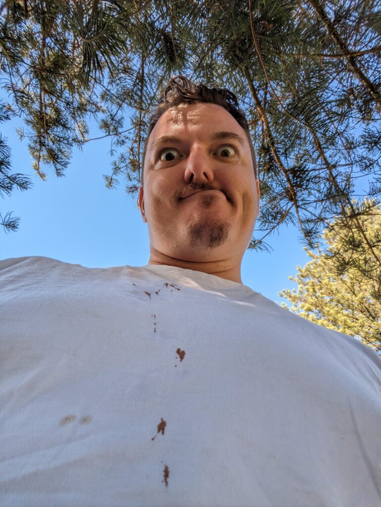 Derpy man with derpy expression with brown drops all down his white tee.