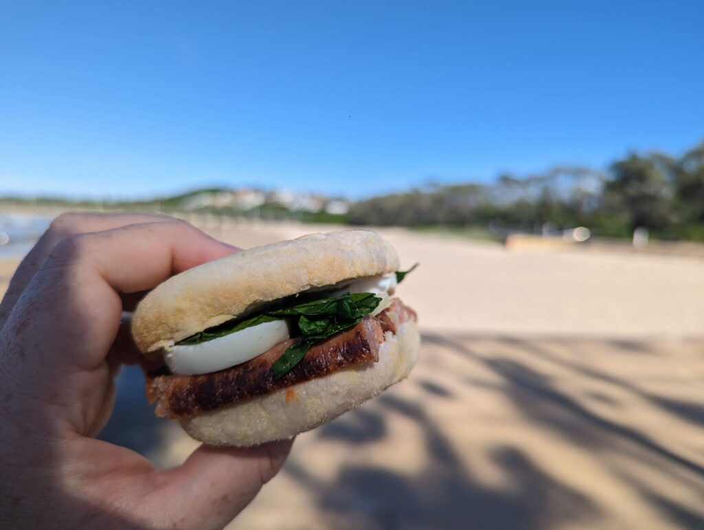 An english muffin with sausage, egg, and greens.