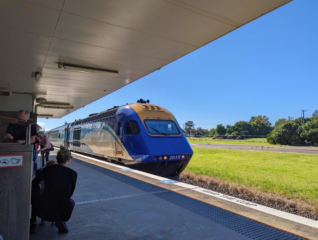 The XPT train pulls into Coffs Harbour station, painted in yellow white and blue.