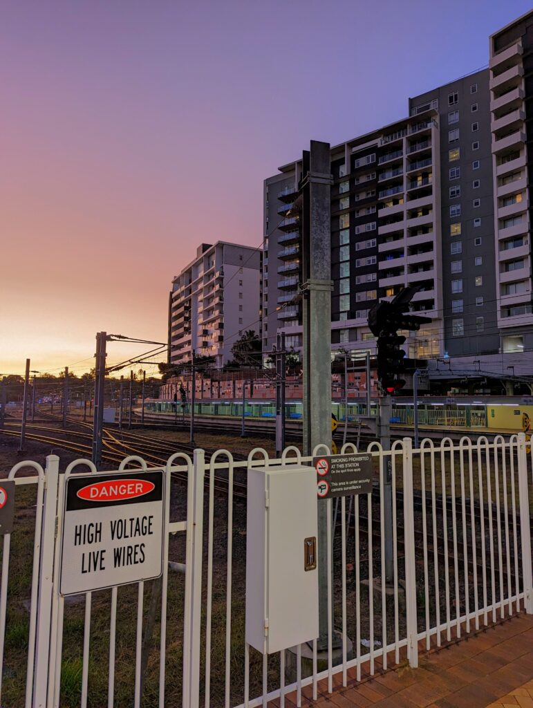 Danger high voltage wires: the end of the train platform at Roma Street. high rises border the rail lines, and the sun sets in yellows, reds and purples.