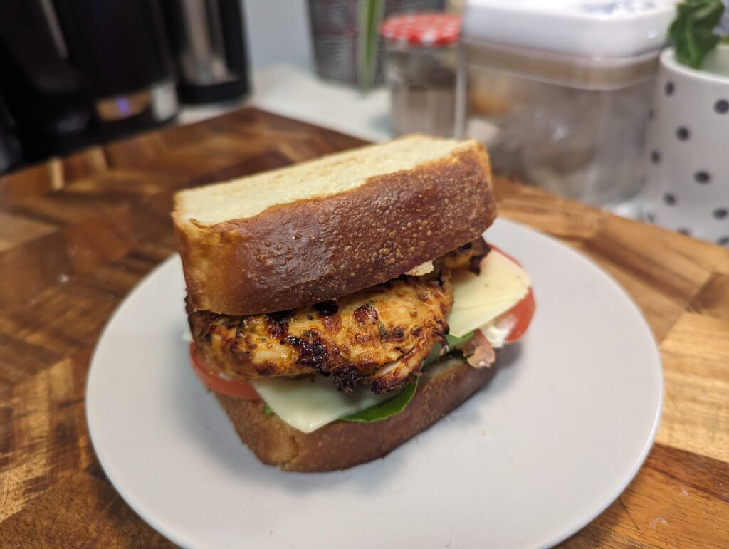 A very thick cut sandwich, with chicken, tomato, cheese and greens.