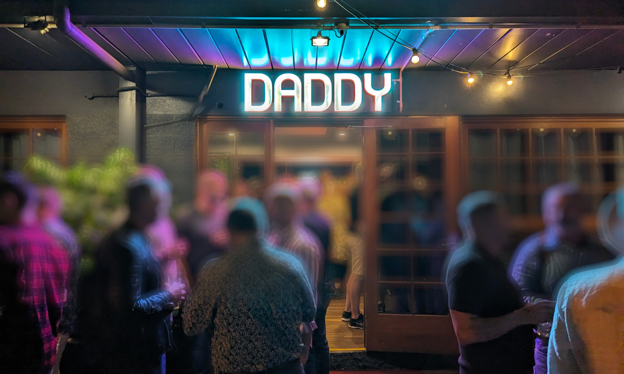 A bar with a neon sign out the front reads "Daddy", and a bunch of people stand around out the front. Their faces are blurred because, y'know, they didn't ask to have their photo taken.